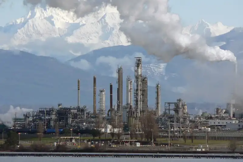Refinería con torres de proceso y vapor al pie de una cordillera